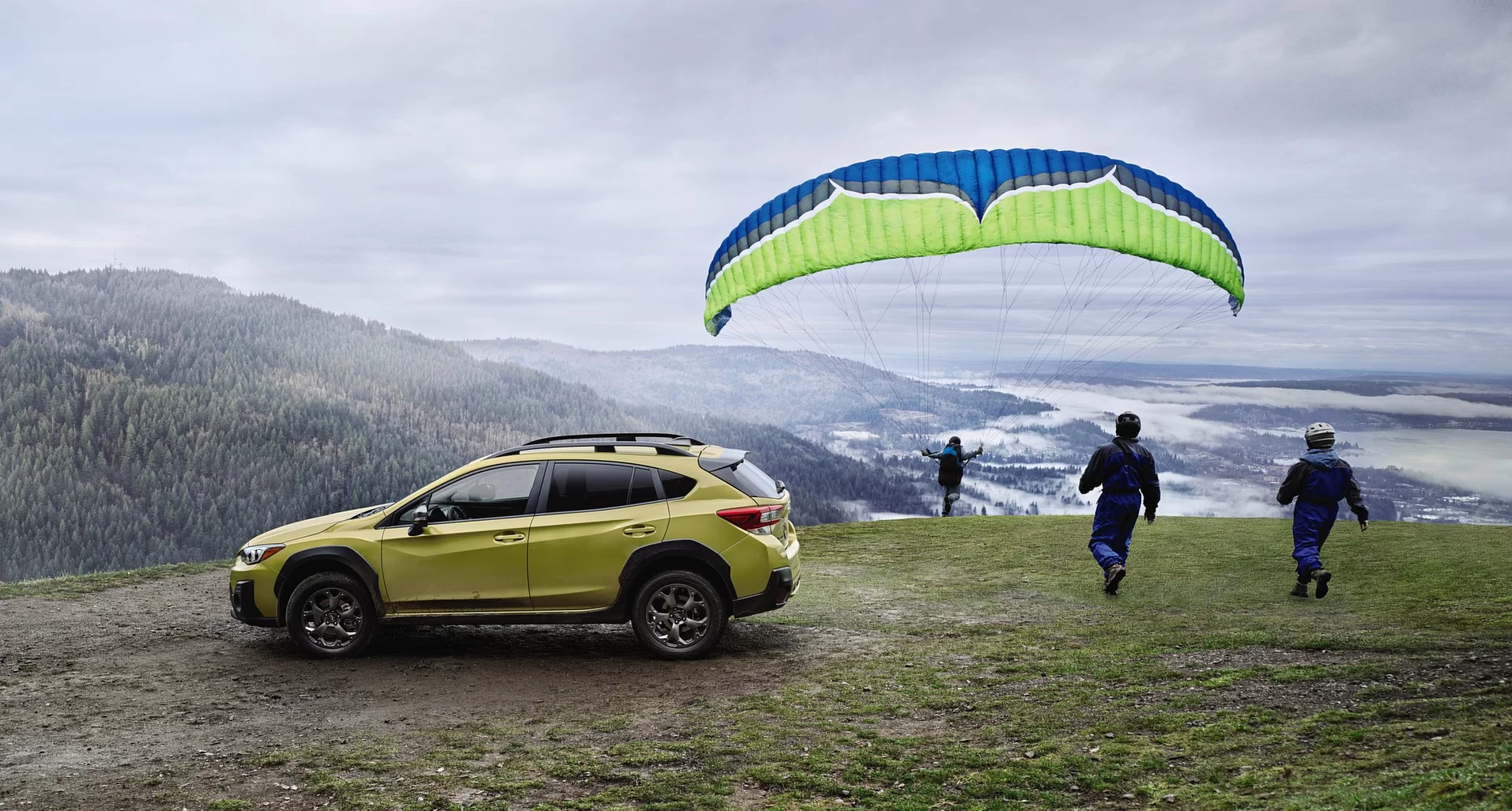 2021-2022 green subaru suv on top of a mountain with people about to do paraglider